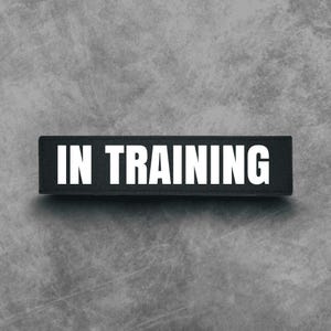May include: Black and white patch with the text "IN TRAINING" in white letters.