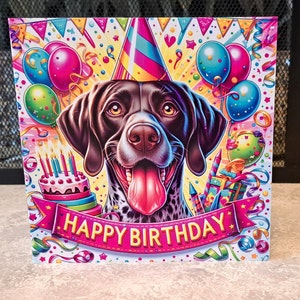 May include: A birthday card featuring a cartoon black and white dog wearing a party hat. The dog is surrounded by colourful balloons, confetti, and the words "Happy Birthday".