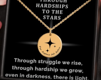 May include: A gold-colored necklace with a round pendant featuring a star design and the words "Per Aspera Ad Astra." The necklace is displayed in a black box with the words "Through Hardships to the Stars" and an inspirational quote.