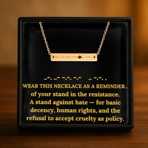 Può includere: Collana dorata con una barra con codice Morse e un piccolo dettaglio nero, su sfondo nero. Il testo recita: "WEAR THIS NECKLACE AS A REMINDER..." (Indossa questa collana come promemoria...)
