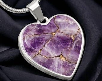 May include: A heart-shaped pendant featuring a purple and white marbled stone pattern with gold-colored veining. The pendant is encased in a smooth silver-toned metal frame and is attached to a matching silver-toned snake chain necklace.