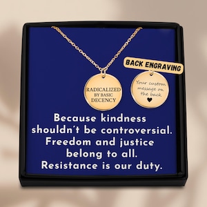 May include: A gold-colored necklace with two round pendants, one engraved with "RADICALIZED BY BASIC DECENCY," and the other with "Your custom message on the back" and a heart. The necklace is displayed in a black box with blue interior, with text that reads "Because kindness shouldn't be controversial."