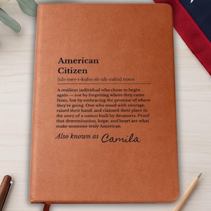 May include: A brown leather-bound journal with the words "American Citizen" and a definition printed on the cover. The definition describes an American as a resilient individual. The name "Camila" is also printed on the cover.