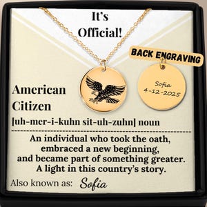 Op de afbeelding: Goudkleurige ketting met een ronde hanger met een adelaarontwerp. De tekst "American Citizen" staat op de kaart. De ketting wordt gepresenteerd in een zwarte doos. De gravure op de achterkant zegt "Sofia 4-12-2025".