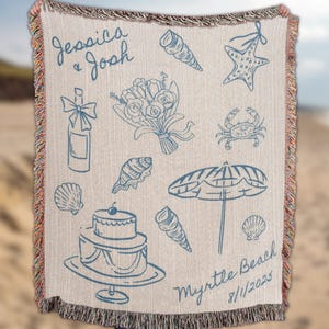 Person holding a custom beach wedding blanket with hand drawn coastal icons including starfish, seashells, champagne glasses, bouquet, umbrella, and wedding cake, displayed against a blurred beach background. Personalized names and date design make it a unique coastal wedding gift, destination wedding keepsake, or custom couple anniversary present.