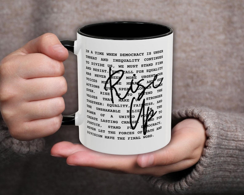 Black and white ceramic mug featuring a bold political message about rising up against injustice and inequality, with “Rise Up” handwritten across the text in black script, symbolizing strength, unity, and resistance.
