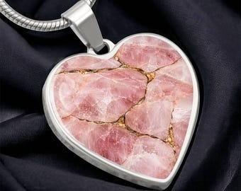 May include: A heart-shaped pendant featuring a mosaic of light pink rose quartz pieces separated by thin, shimmering gold-colored veins. The pendant is encased in a smooth silver-toned metal frame and hangs from a matching silver-toned snake chain.
