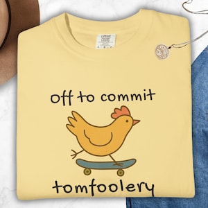 Butter Comfort Colors t-shirt with a quirky chicken riding a skateboard and the phrase ‘off to commit tomfoolery’ in playful handwritten-style text. Funny silly animal design with cottagecore and Gen Z meme vibes.
