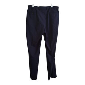 May include: Navy blue dress pants hanging on a white hanger. The pants have a button and pockets. The fabric appears to be a medium-weight material, suitable for various occasions. The pants are wrinkle-free.