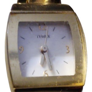 May include: A gold-toned Timex watch with a rectangular face. The watch has a white dial with black hour markers and hands. The Timex logo is visible. The watch band is a dark brown color.