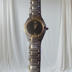 May include: A silver and gold two-tone watch with a black face and diamond accents around the bezel. The watch has Roman numeral hour markers and a gold second hand.