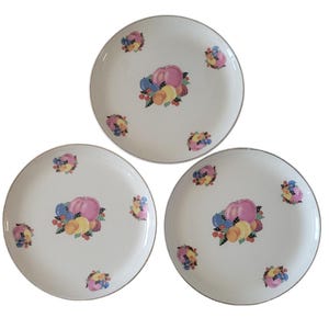 May include: Three white ceramic plates with a gold rim. Each plate features a colorful fruit design with pink, yellow, orange, blue, and green hues.