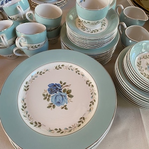 Peut inclure: Un ensemble de vaisselle vintage en porcelaine bleu et blanc à fleurs. L'ensemble comprend des assiettes, des tasses et des soucoupes. Le motif floral présente des roses bleues et des feuilles vertes.