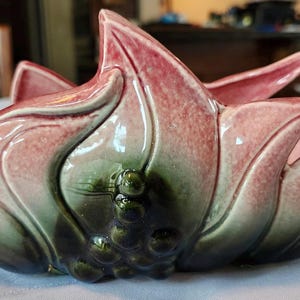 May include: A ceramic flower-shaped bowl with a glossy finish. The bowl features a blend of pink, green, and dark blue hues. The design resembles a blooming flower, with petal-like edges. The bowl is likely used for decorative purposes.