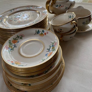 May include: A set of vintage floral china teacups and saucers with gold trim. The set includes a teapot, creamer, and a stack of dinner plates.