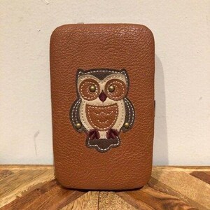 May include: A brown, rectangular case with a textured surface. The case features an appliqued owl design in shades of brown, cream, and burgundy. The owl has large, round eyes and is centered on the front of the case.