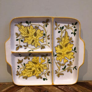 Puede incluir: Una fuente rectangular dividida con fondo blanco y borde amarillo. La fuente presenta un diseño de hojas en amarillo, marrón y verde. La fuente tiene dos asas laterales.