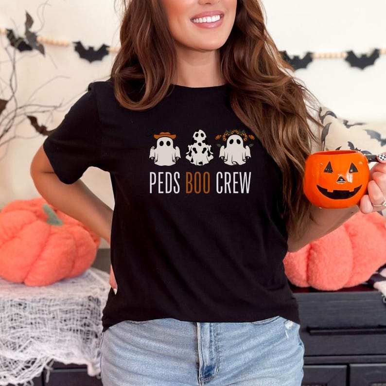 May include: A black t-shirt with three white ghosts wearing Halloween costumes. The text 'PEDS BOO CREW' is printed on the shirt.