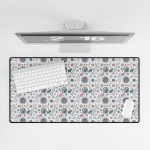May include: A rectangular mousepad with a black border and a white background. The mousepad features a repeating pattern of blue, pink, and gray circular and organic shapes. A white keyboard and mouse are on the mousepad.
