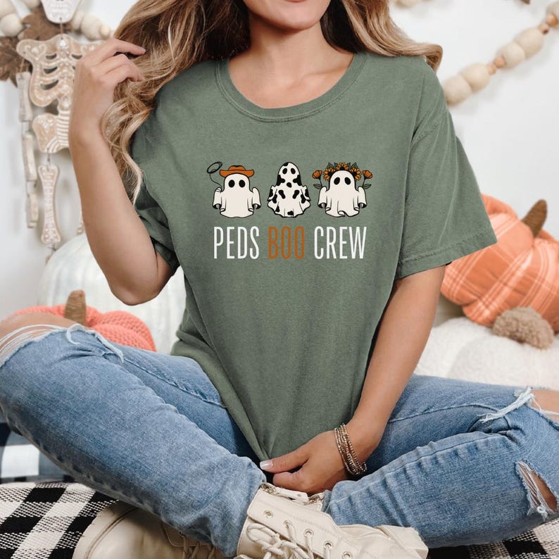 Puede incluir: Una camiseta verde con un gr&aacute;fico de tres fantasmas con diferentes disfraces. El texto "PEDS BOO CREW" est&aacute; impreso debajo de los fantasmas.