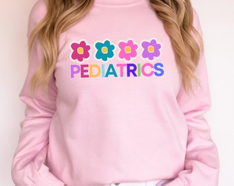 May include: A pink sweatshirt with a colorful graphic of four flowers and the word "PEDIATRICS" in rainbow letters.