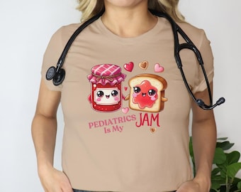 May include: A tan t-shirt featuring a cartoon design of a jam jar and a slice of toast, both with smiling faces. The text "Pediatrics Is My Jam" is printed below the images. A stethoscope is around the neck.