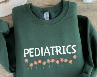 May include: A dark green sweatshirt with the word "PEDIATRICS" printed in white. A row of pink flowers with green stems are printed below the word.