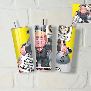 Puede incluir: Vaso aislado amarillo y plateado con una caricatura de un hombre con traje que sostiene un letrero que dice "ETHICS VIOLATION LAWSUIT v. TRUMP ORGANIZA PP". El vaso también tiene el texto "FUND TAX" y "FUNDED BY U.S. TAX PAYERS".