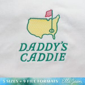 May include: White embroidered design of a golf course with a flag and the text "Daddy's Caddie" in green.