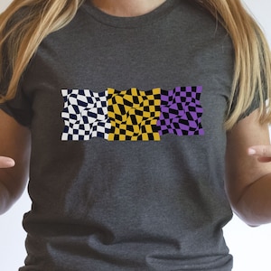 May include: A gray t-shirt with a checkered pattern design in black, yellow, and purple. The checkered pattern is a stylized representation of a checkered flag.