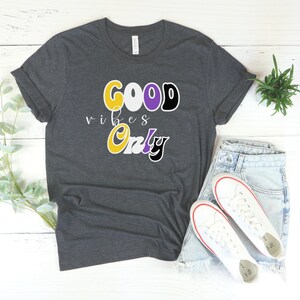 May include: A dark gray t-shirt with the text "GOOD vibes Only" in yellow, white, purple, and black lettering.