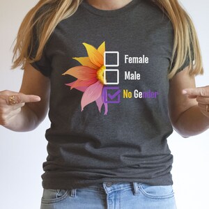 May include: Dark gray t-shirt featuring a colorful flower design with the text "Female", "Male", and "No Gender". The "No Gender" option is checked. The shirt is a crew neck.