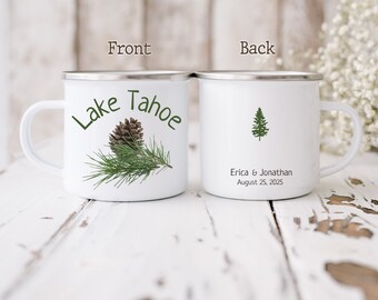 May include: Two white enamel camping mugs with a pine tree design. The front mug says "Lake Tahoe" with a pine cone and pine needles. The back mug says "Erica & Jonathan August 25, 2025".