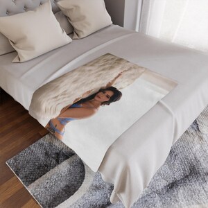 May include: A white blanket with a woman in blue lingerie. The blanket is on a bed with white sheets and pillows. A gray rug is visible in the foreground.