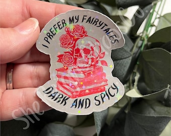 May include: A holographic sticker featuring a red skull resting on a stack of red books, surrounded by red roses. The text "I PREFER MY FAIRYTALES DARK AND SPICY" is printed in black lettering around the central illustration of the skull and books.
