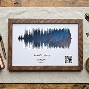 May include: A rectangular wooden frame containing a white print with a blue and black galaxy-patterned sound wave graphic. The text reads David & Mary, Stand By Me, and 07.04.2021, accompanied by a small black and white QR code in the bottom right corner.