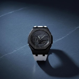 May include: A black and white wristwatch with a dark grey face. The watch has a black bezel and a white strap. The watch face displays the time. The watch is on a dark blue surface.