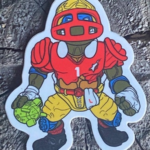 以下が含まれることがあります： 赤、黄、青の漫画キャラクターがフットボールのユニフォームとヘルメットを着ています。キャラクターは左手に緑色の手榴弾を持っています。キャラクターは「1」の番号が書かれた赤いジャージを着ています。キャラクターは黄色のズボンと青と赤の靴下を履いています。キャラクターは黒い靴を履いています。キャラクターは木製の表面に立っています。