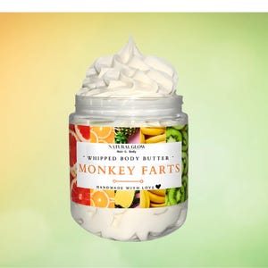 May include: A jar of whipped body butter with a white, fluffy top. The jar has a label with the text "Monkey Farts" and a colorful design of fruit slices. The product is handmade with love.