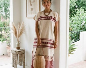 May include: A beige and burgundy patterned dress with a woven basket bag. The dress has short sleeves and a fringed hem. The bag is light brown with a leather handle. The dress is paired with brown sandals.