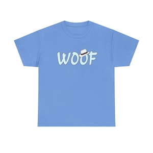 May include: A light blue t-shirt with the word "WOOF" in a playful, light blue font. The "O" is topped with a small, white fedora hat. The shirt is a solid color, with a crew neck.