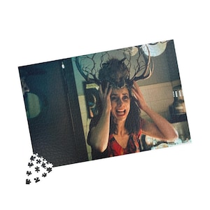 Op de afbeelding: Een rechthoekige puzzelstukjes-assemblage met een scène van een persoon met een verwarde uitdrukking die een groot, donker, vertakt gewei als hoofdtooi draagt. De afbeelding heeft een donker, sfeervol kleurenpalet met diepe schaduwen.