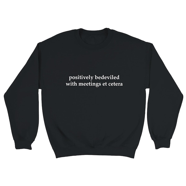May include: Black sweatshirt with the phrase "positively bedeviled with meetings et cetera" printed in white. The long-sleeved crew neck top is made of a soft material.