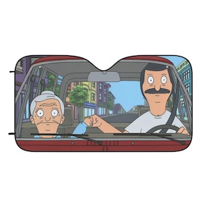 May include: A rectangular car sunshade featuring a cartoon illustration of a man with a mustache and an elderly person with gray hair sitting in the front seats of a vehicle, performing a fist bump while driving through a city street.