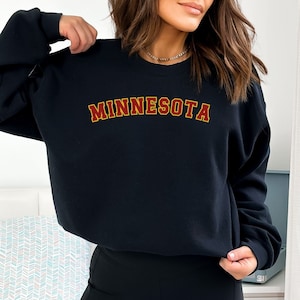May include: Black sweatshirt with a gold outline and red lettering that says "MINNESOTA".