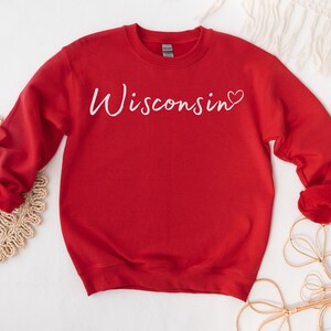 May include: Red sweatshirt with white text that says "Wisconsin" with a small heart after the word.