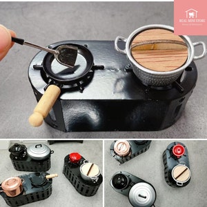 Puede incluir: Miniatura de cocina negra con sartén, olla y espátula. La sartén tiene un mango de madera. La olla tiene una tapa de madera. La estufa tiene dos quemadores. La imagen muestra un primer plano del juego de cocina en miniatura.