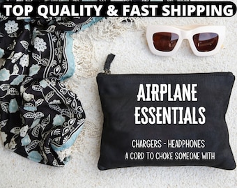 May include: A black zippered pouch with the white text AIRPLANE ESSENTIALS, CHARGERS - HEADPHONES, A CORD TO CHOKE SOMEONE WITH, accompanied by a black and light blue floral patterned scarf with fringe and white-framed sunglasses.