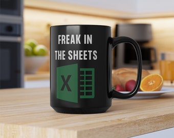 Puede incluir: Taza de café negra con texto blanco que dice "Freak in the sheets" y un logotipo verde de Microsoft Excel.