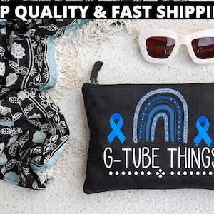 以下が含まれることがあります： 虹のデザインと2本の青いリボンが付いた黒いキャンバス製のジッパー付きポーチ。虹の下に白い文字で「G-TUBE THINGS」と印刷されています。
